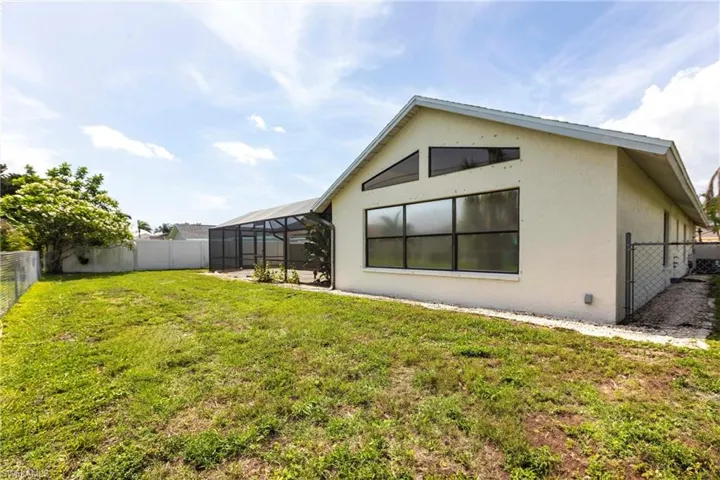 Back of house with stucco siding, a fenced backyard, and glass enclosure