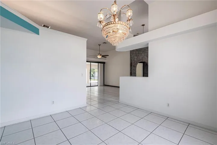 Spare room featuring a chandelier, light tile patterned flooring, a ceiling fan, a fireplace, and crown molding