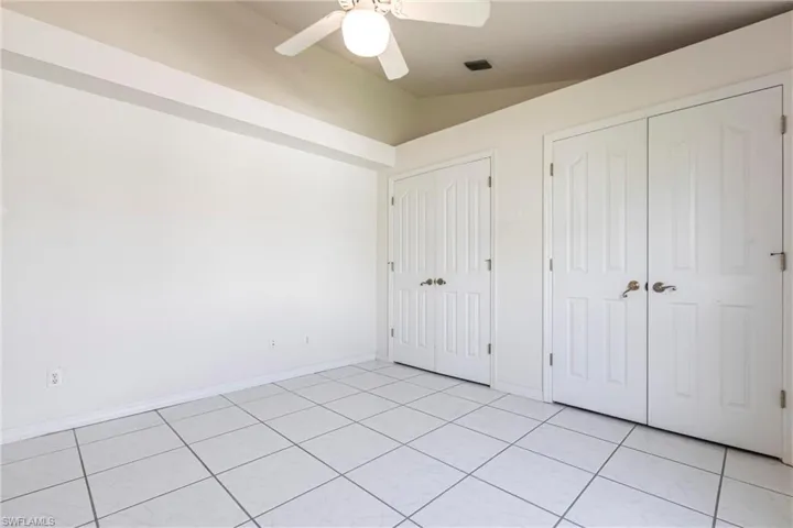 Unfurnished bedroom featuring two closets, vaulted ceiling, light tile patterned floors, and a ceiling fan