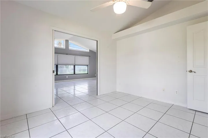 Unfurnished room with lofted ceiling, ceiling fan, and light tile patterned flooring