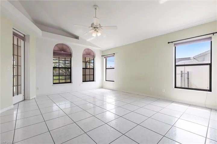 Tiled empty room featuring lofted ceiling, plenty of natural light, and ceiling fan