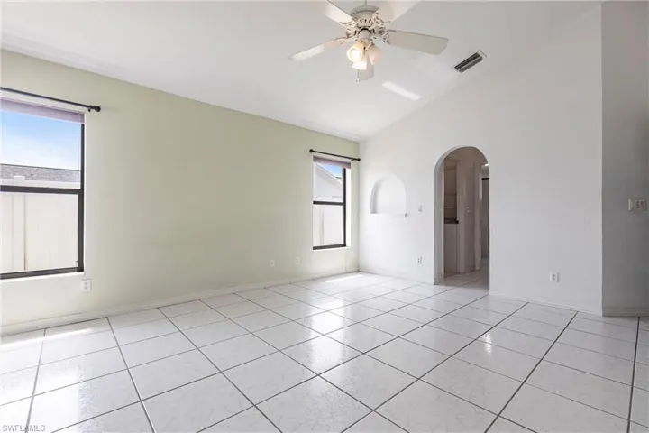 Unfurnished room with arched walkways, plenty of natural light, a ceiling fan, lofted ceiling, and light tile patterned floors