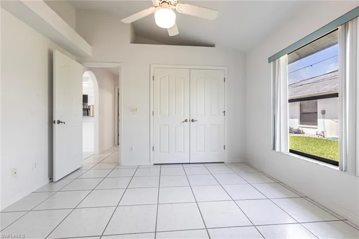 Unfurnished bedroom featuring vaulted ceiling, arched walkways, a closet, light tile patterned flooring, and a ceiling fan