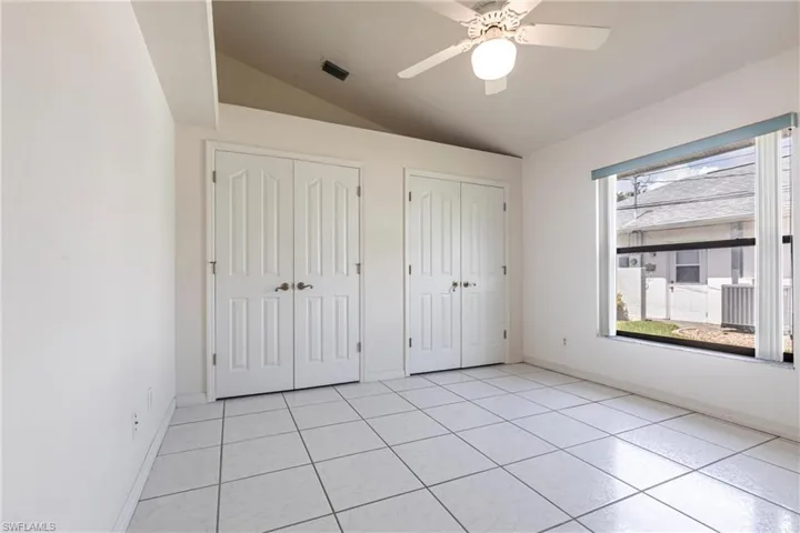 Unfurnished bedroom with two closets, lofted ceiling, light tile patterned floors, and a ceiling fan