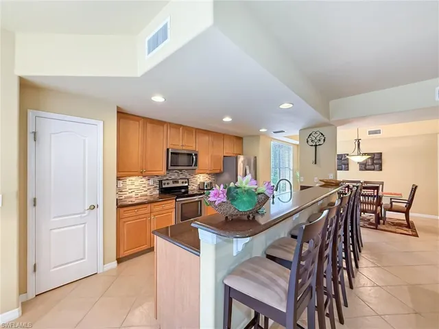 Kitchen featuring stainless steel appliances, visible vents, tasteful backsplash, dark countertops, and a kitchen bar