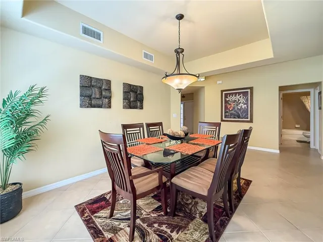 Dining area featuring light tile patterned floors, baseboards, visible vents, and a tray ceiling