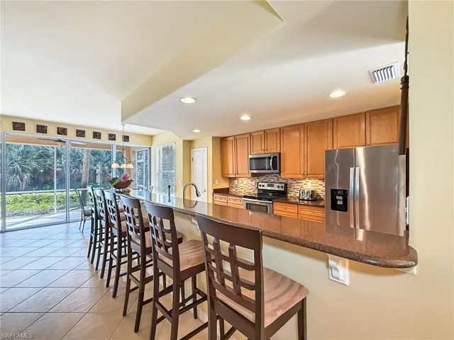 Kitchen featuring a breakfast bar area, light tile patterned floors, visible vents, decorative backsplash, and appliances with stainless steel finishes