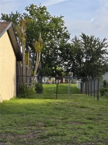 Rear yard featuring a chain link fence, grass, and mature trees
