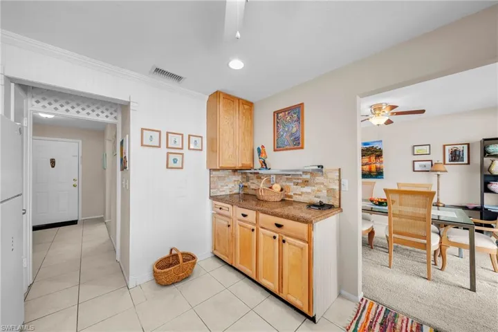 Kitchen featuring decorative backsplash, a ceiling fan, light tile patterned flooring, light wood finish cabinetry, and dark stone countertops