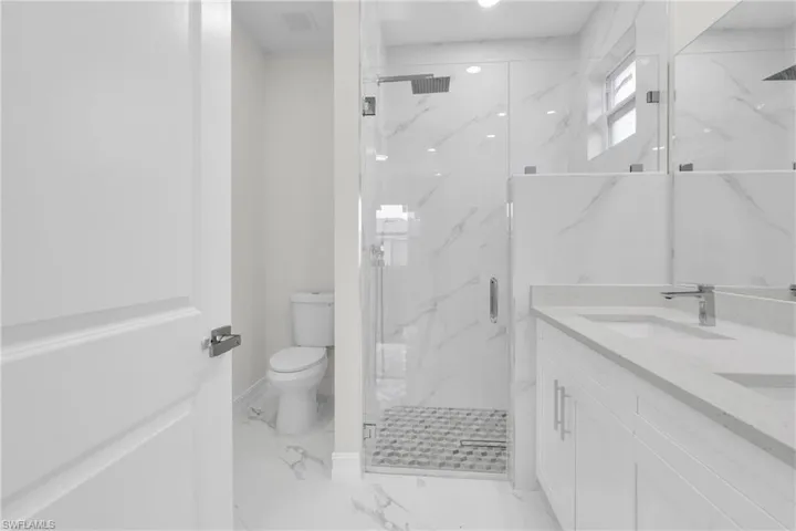 Bathroom featuring marble finish floors, a marble finish shower, and double vanity