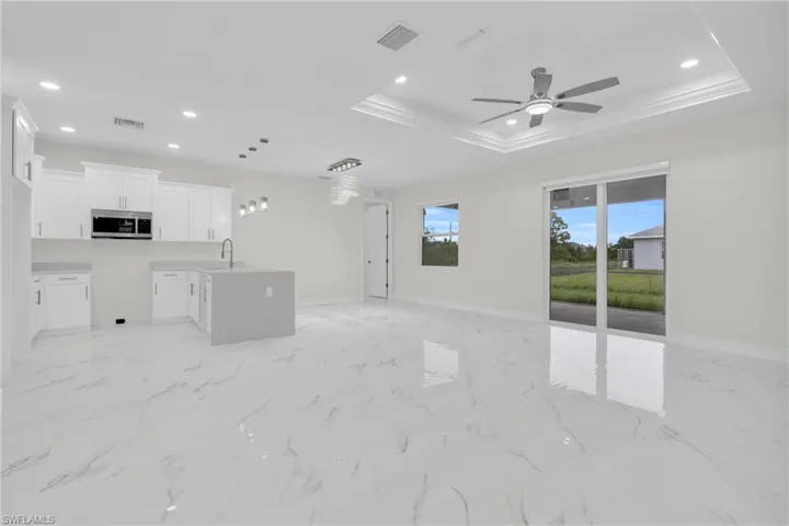 Unfurnished living room featuring a tray ceiling, a ceiling fan, recessed lighting, light marble finish floors, and ornamental molding