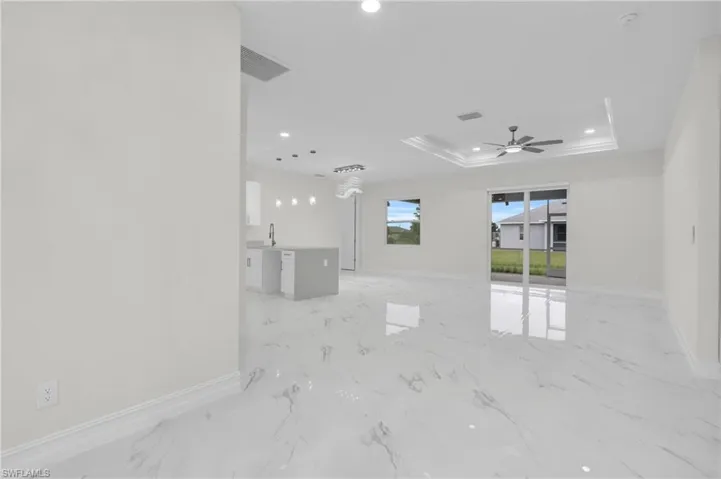 Unfurnished living room featuring a tray ceiling, a ceiling fan, recessed lighting, and light marble finish floors