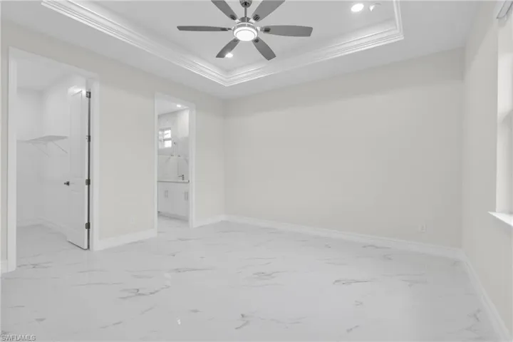 Unfurnished bedroom featuring a spacious closet, light marble finish flooring, ornamental molding, a raised ceiling, and recessed lighting