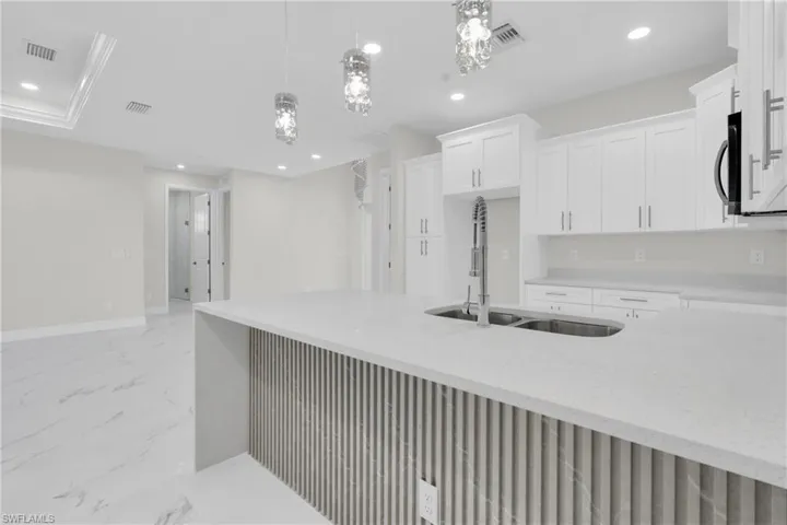 Kitchen featuring light marble finish floors, light stone counters, white cabinets, recessed lighting, and decorative light fixtures