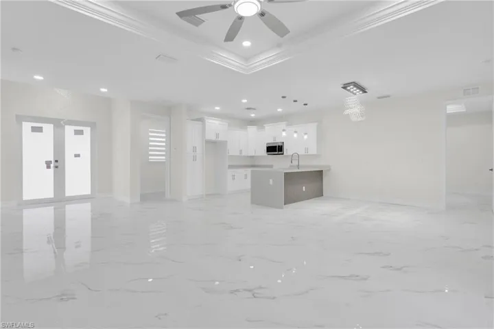 Unfurnished living room featuring a raised ceiling, light marble finish floors, ceiling fan, recessed lighting, and ornamental molding