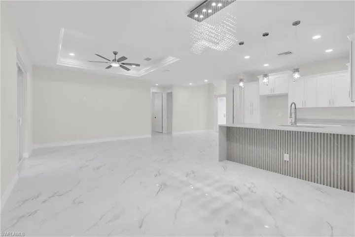 Unfurnished living room with recessed lighting, light marble finish floors, ceiling fan, and a raised ceiling