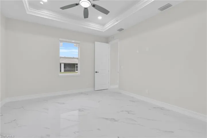 Empty room with a tray ceiling, crown molding, a ceiling fan, marble look tile flooring, and recessed lighting
