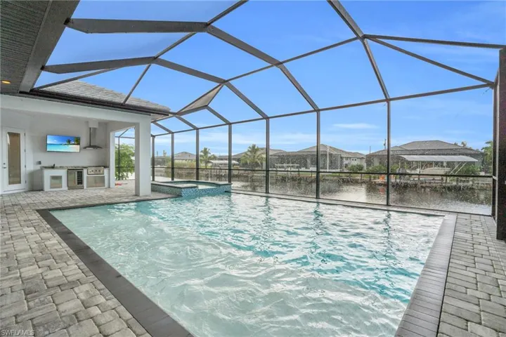 View of pool with an outdoor kitchen, an in ground hot tub, a lanai, a patio area, and a water view