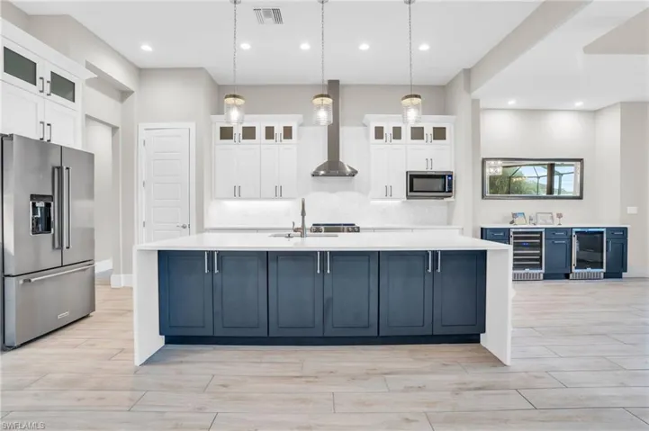 Kitchen with wine cooler, a large island, decorative light fixtures, and stainless steel appliances