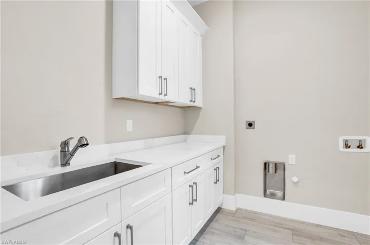 Clothes washing area with hookup for a washing machine, hookup for an electric dryer, light wood-type flooring, sink, and cabinets