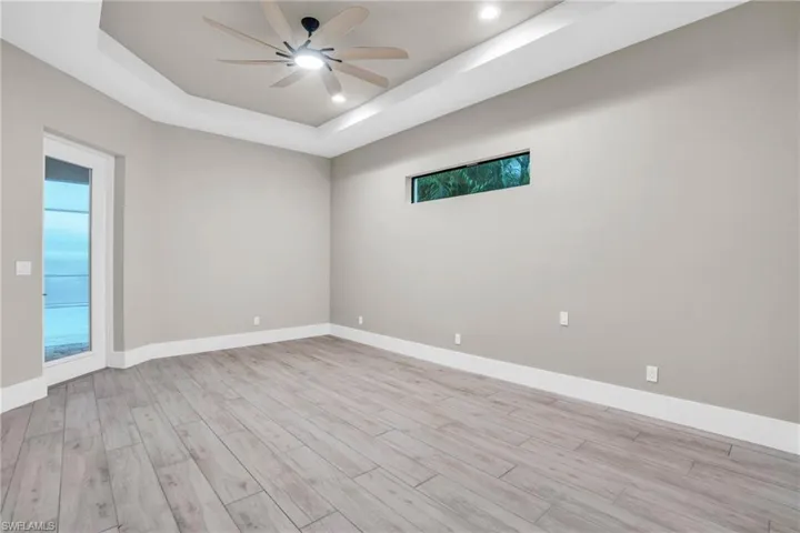 Unfurnished room with ceiling fan, a tray ceiling, and light hardwood / wood-style flooring