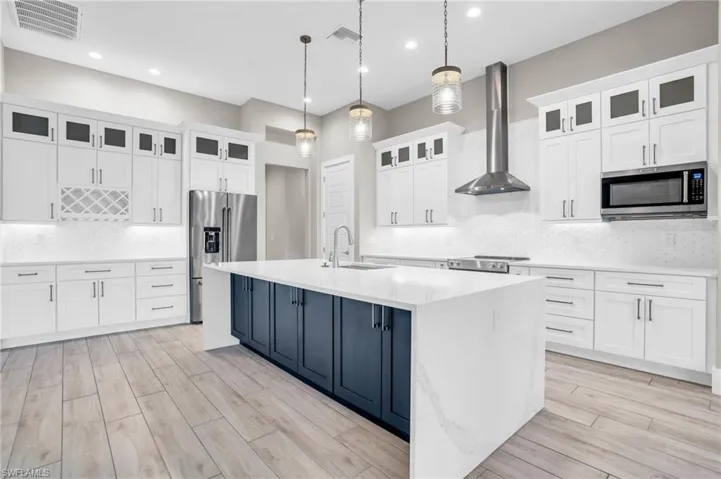 Kitchen with a kitchen island with sink, wall chimney range hood, stainless steel appliances, sink, and white cabinets
