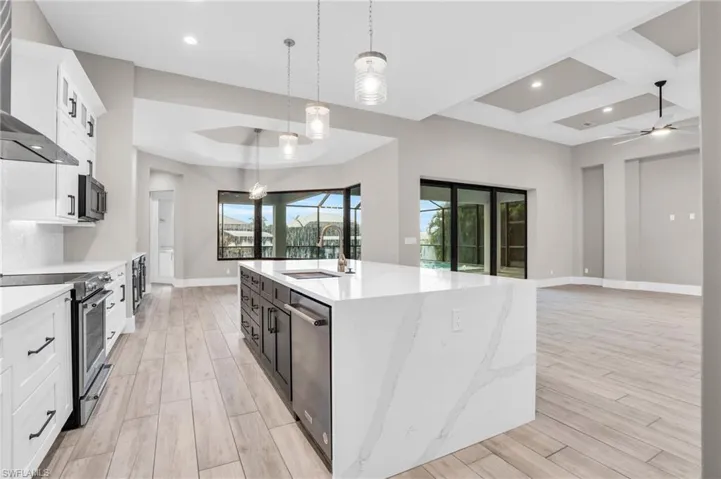 Kitchen with light hardwood / wood-style flooring, stainless steel appliances, decorative light fixtures, and an island with sink