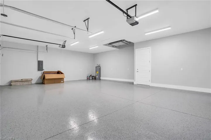 Garage featuring electric panel, electric water heater, and a garage door opener