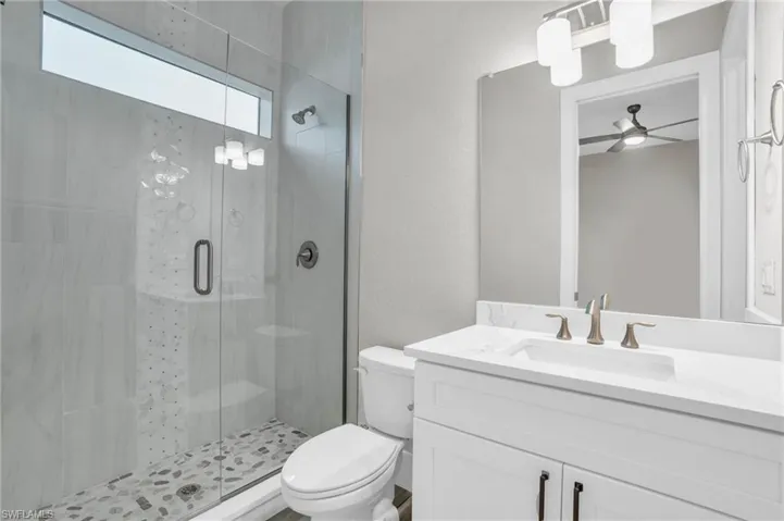 Bathroom featuring vanity, toilet, a shower with shower door, and ceiling fan