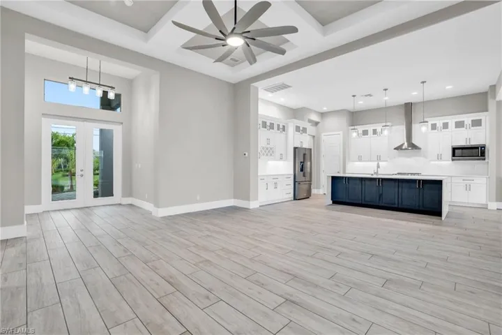 Kitchen with wall chimney range hood, white cabinetry, light wood-type flooring, stainless steel appliances, and decorative light fixtures