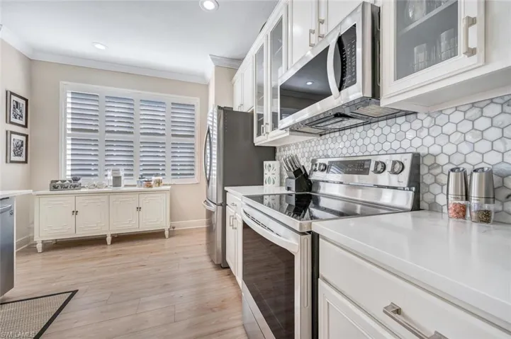 Kitchen featuring light hardwood / wood-style flooring, stainless steel appliances, tasteful backsplash, white cabinetry, and ornamental molding