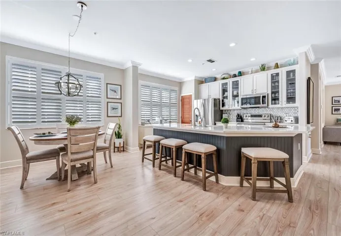 Kitchen featuring light hardwood / wood-style flooring, tasteful backsplash, stainless steel appliances, white cabinets, and a kitchen island with sink