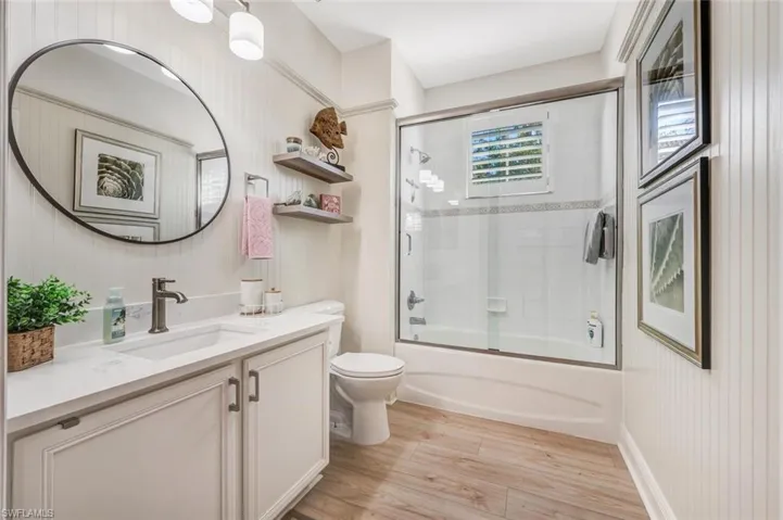 Full bathroom with hardwood / wood-style floors, vanity, toilet, and enclosed tub / shower combo