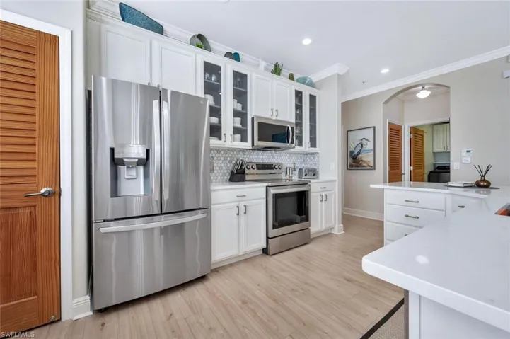 Kitchen featuring crown molding, tasteful backsplash, light wood-type flooring, white cabinetry, and appliances with stainless steel finishes