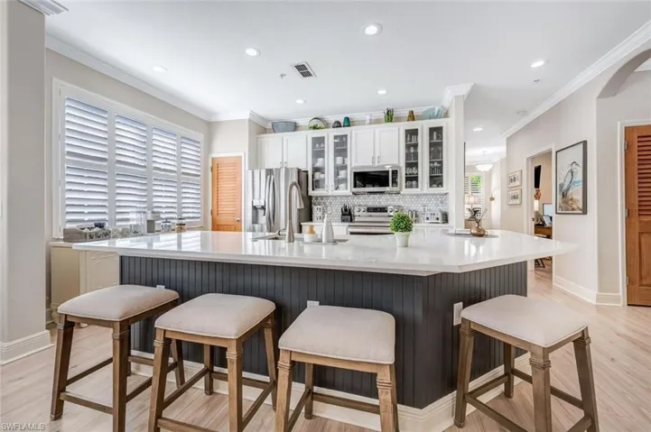 Kitchen with backsplash, appliances with stainless steel finishes, a breakfast bar area, and crown molding