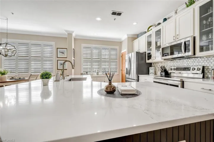 Kitchen featuring light stone countertops, stainless steel appliances, backsplash, pendant lighting, and sink