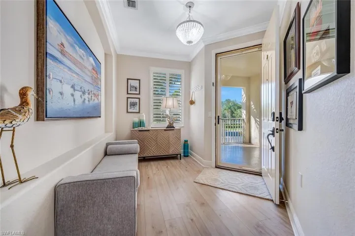 Entrance foyer with ornamental molding, light hardwood / wood-style floors, and an inviting chandelier