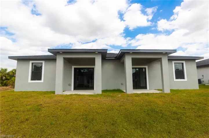 Back of house with stucco siding, a lawn, and a patio area