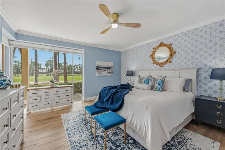 Bedroom with crown molding, wallpapered walls, light wood-style flooring, an accent wall, and ceiling fan