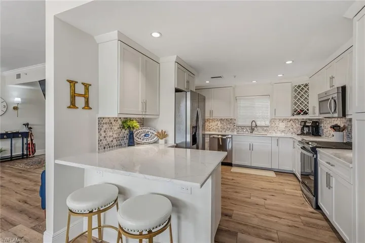 Kitchen with a kitchen breakfast bar, stainless steel appliances, light wood finished floors, light stone countertops, and a peninsula