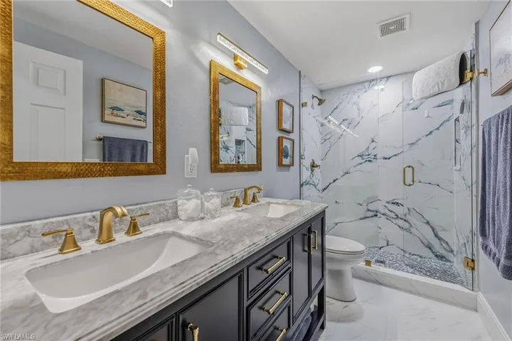 Full bathroom with a marble finish shower, double vanity, light marble finish floors, and recessed lighting