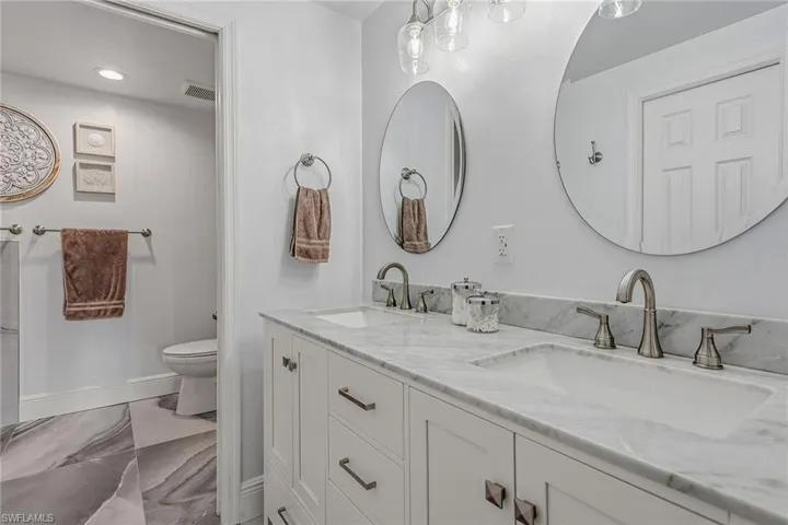 Full bath with double vanity and light marble finish floors