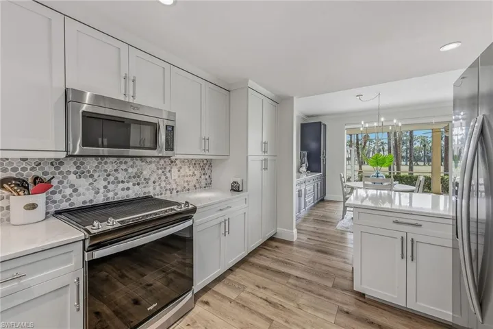 Kitchen featuring appliances with stainless steel finishes, white cabinetry, a chandelier, light stone counters, and recessed lighting