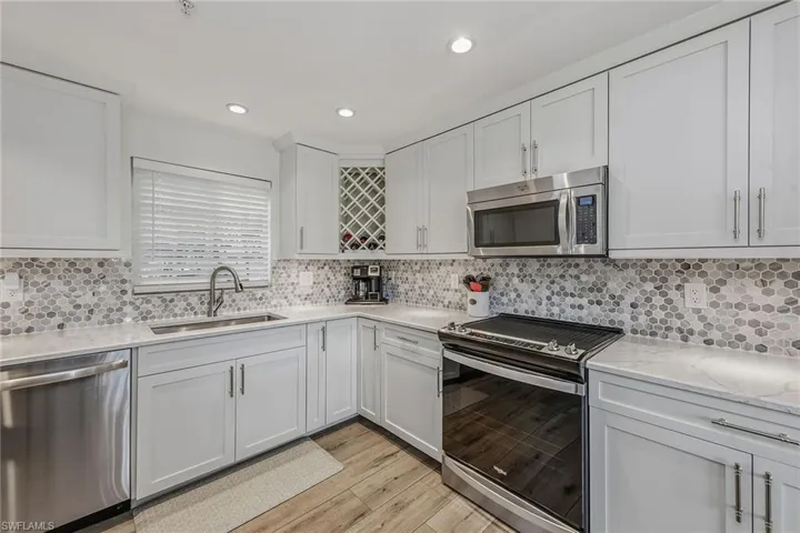 Kitchen with stainless steel appliances, light stone counters, recessed lighting, light wood finished floors, and decorative backsplash