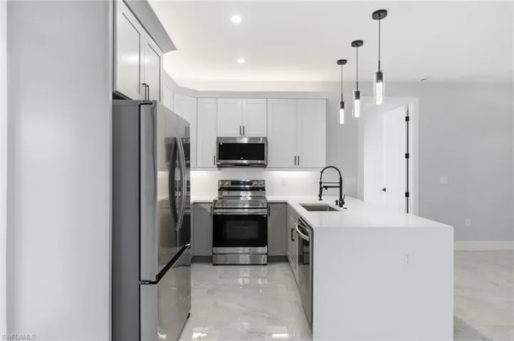 Kitchen featuring a peninsula, stainless steel appliances, light stone countertops, white cabinets, and hanging light fixtures