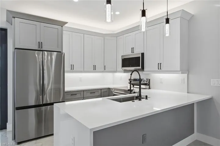 Kitchen with stainless steel appliances, a peninsula, hanging light fixtures, light stone countertops, and gray cabinets