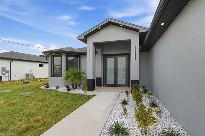 Entrance to property with french doors, stucco siding, a yard, and roof with shingles