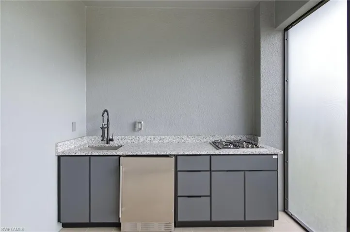 Indoor wet bar featuring gray cabinets, light stone countertops, stainless steel appliances, and a textured wall