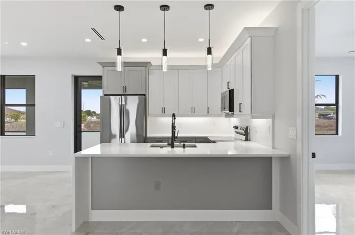 Kitchen featuring a peninsula, stainless steel appliances, light stone countertops, and decorative light fixtures