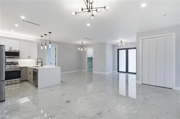 Kitchen with suspended lighting, stainless steel appliances, open floor plan, a peninsula, and light stone counters